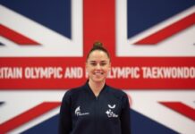 Paralympian Beth Munro smiling in front of GB Flag, which reads 'Britain Olympic and Paralympic Taekwondo'.