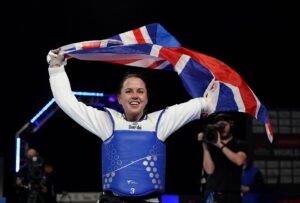 Great Britain's Beth Munro celebrates winning gold against Elena Savinskaya in the Women's 65kg final by holding the GB flag aloft, on day one of the 2023 World Taekwondo Grand Prix Final at the Manchester Regional Arena, Manchester.