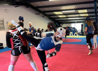 Taekwondo trainers in action at Whiston Taekwondo. One woman executes a high kick.