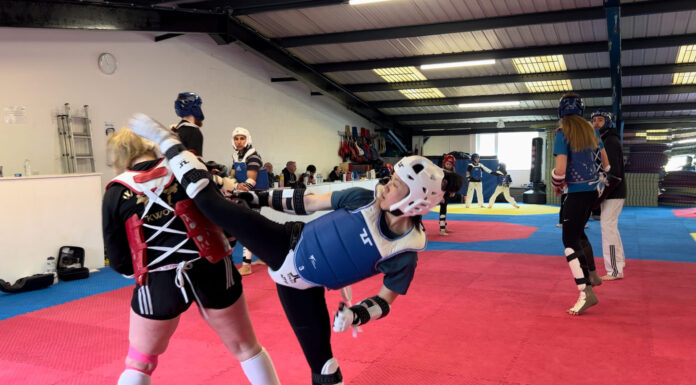 Taekwondo trainers in action at Whiston Taekwondo. One woman executes a high kick.