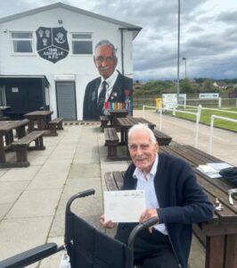 Ashville FC founder John Dennett MBE poses with his mural, painted by local artist Paul Curtis in 2023 (Image courtesy of Ashville FC)